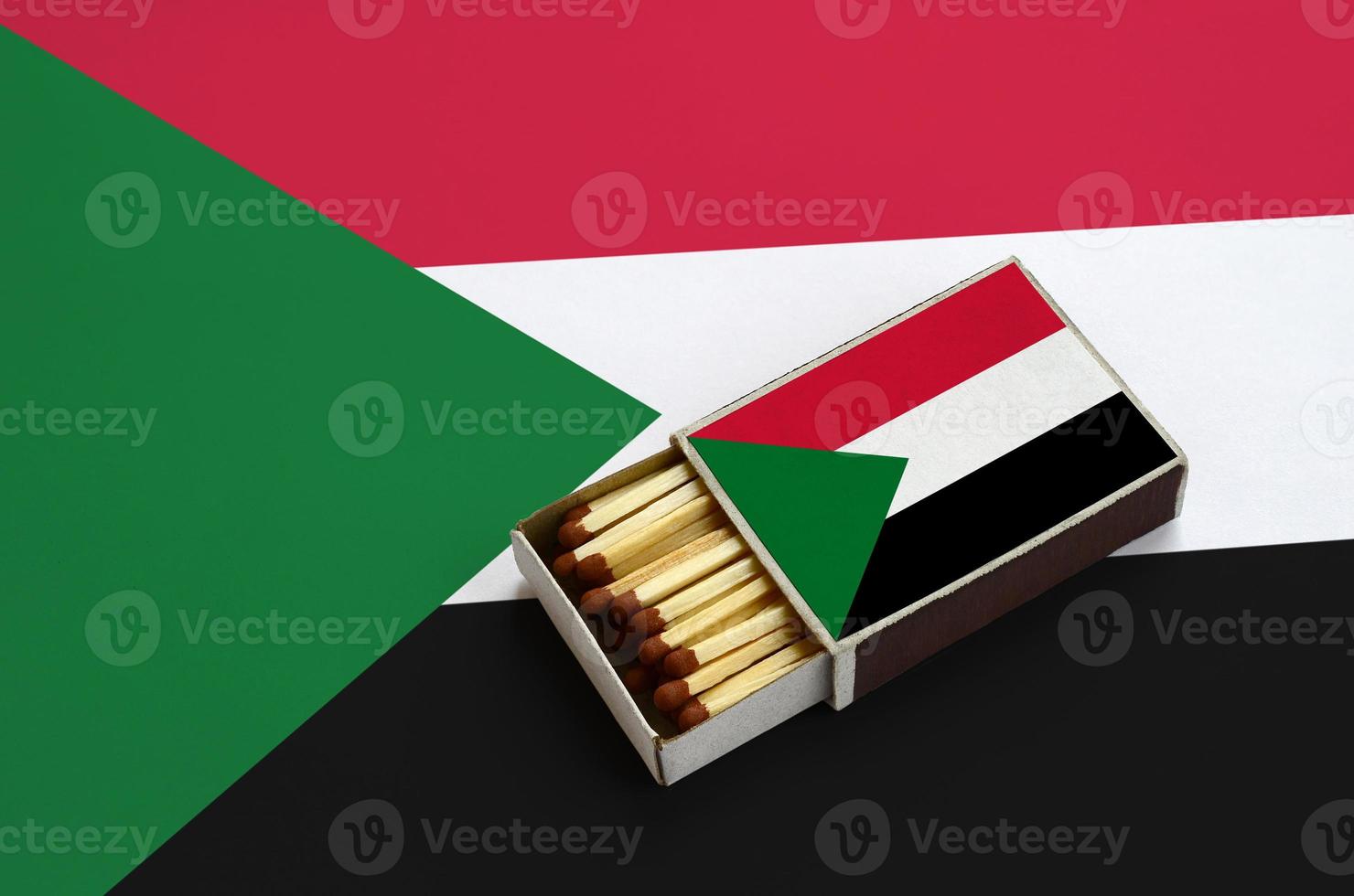 Sudan flag is shown in an open matchbox, which is filled with matches and lies on a large flag photo