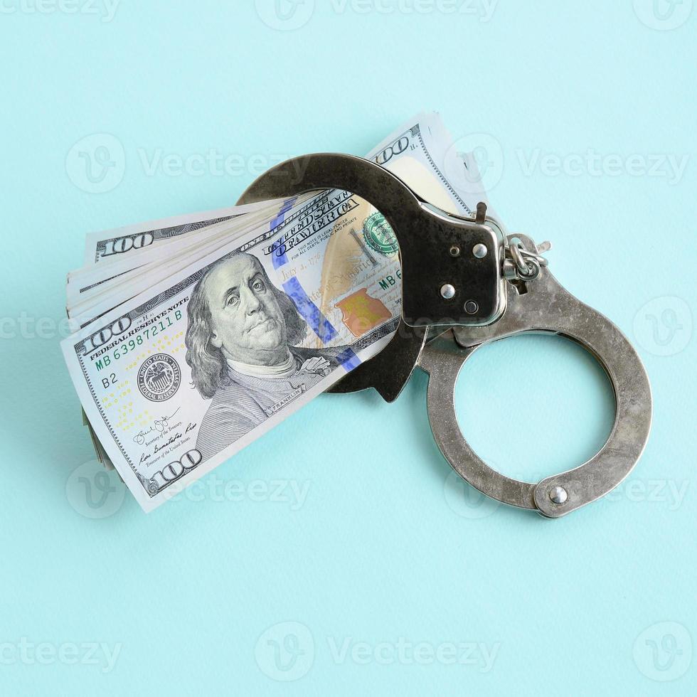 Silver police handcuffs and hundred dollar bills lies on light blue background photo