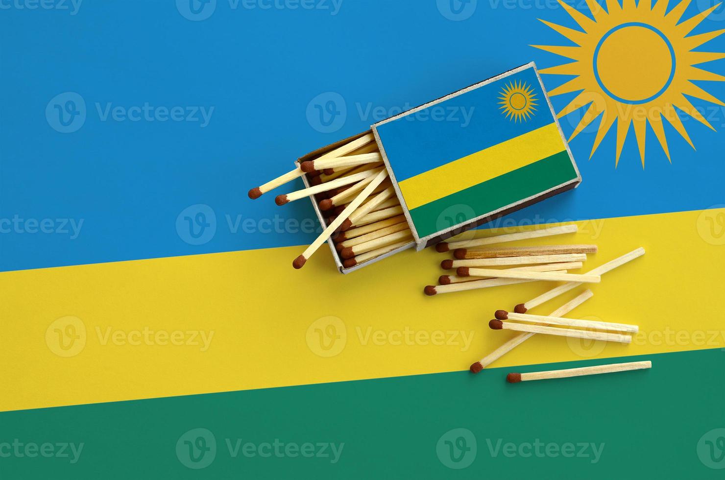 Rwanda flag is shown on an open matchbox, from which several matches fall and lies on a large flag photo