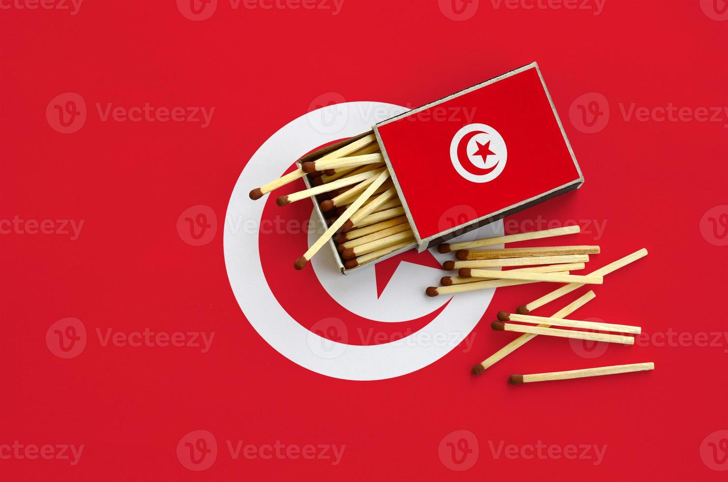 Tunisia flag is shown on an open matchbox, from which several matches fall and lies on a large flag photo