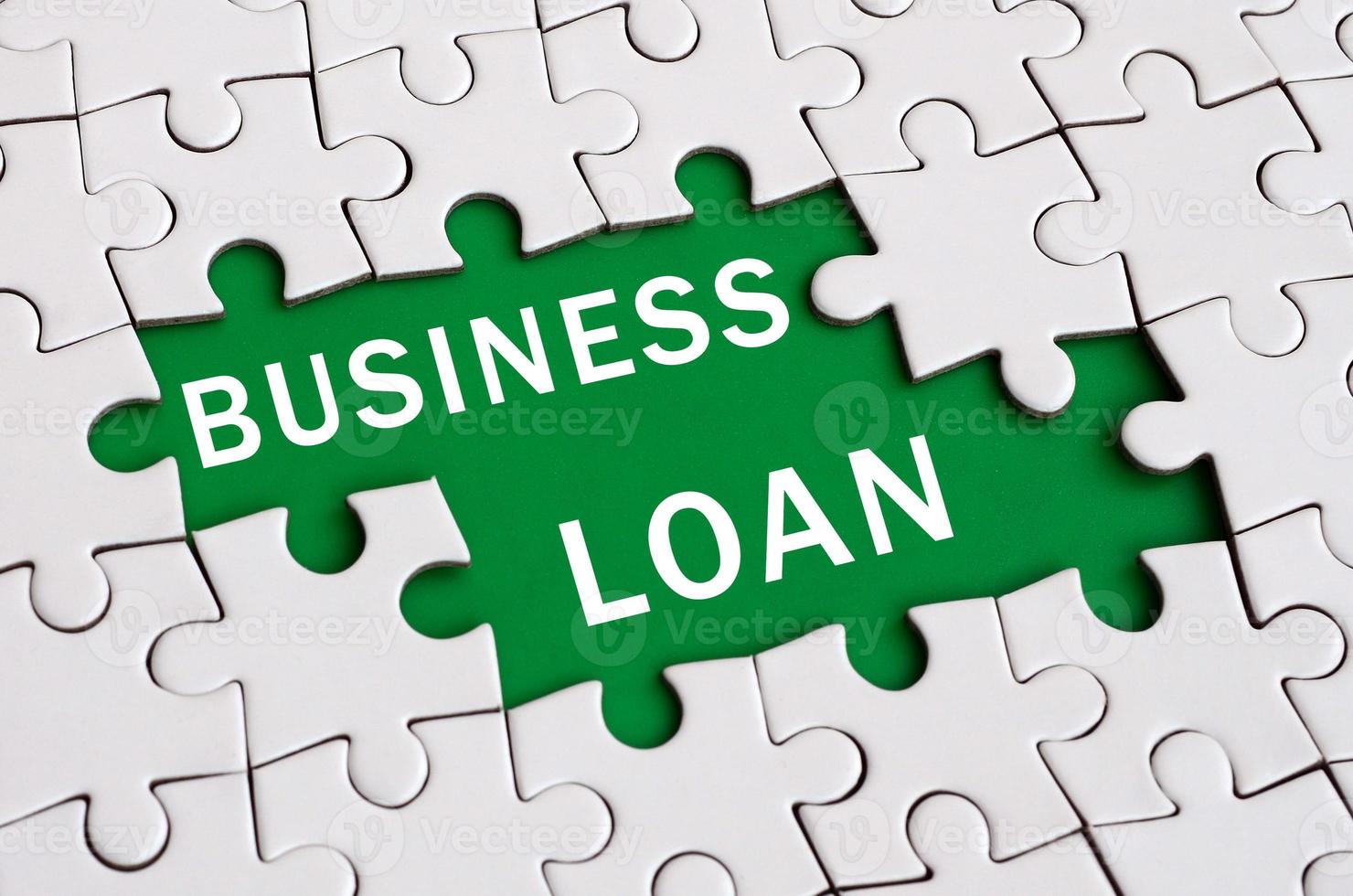 White jigsaw puzzle in assembled state with missing elements forming a green space with white inscription. Business loan photo