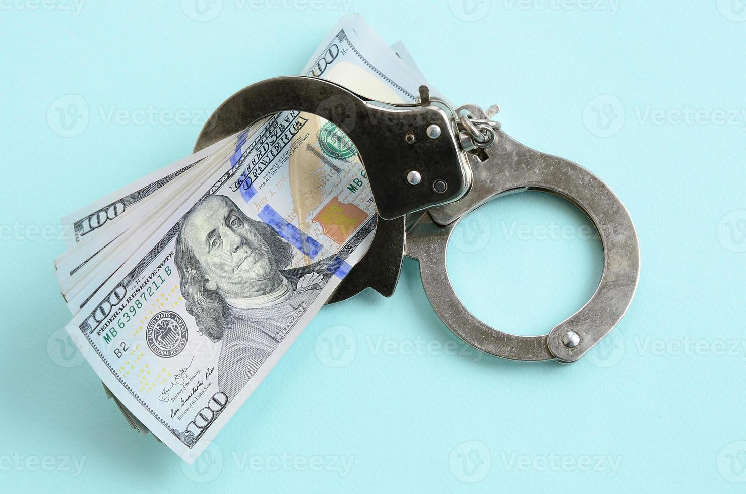 Silver police handcuffs and hundred dollar bills lies on light blue background photo