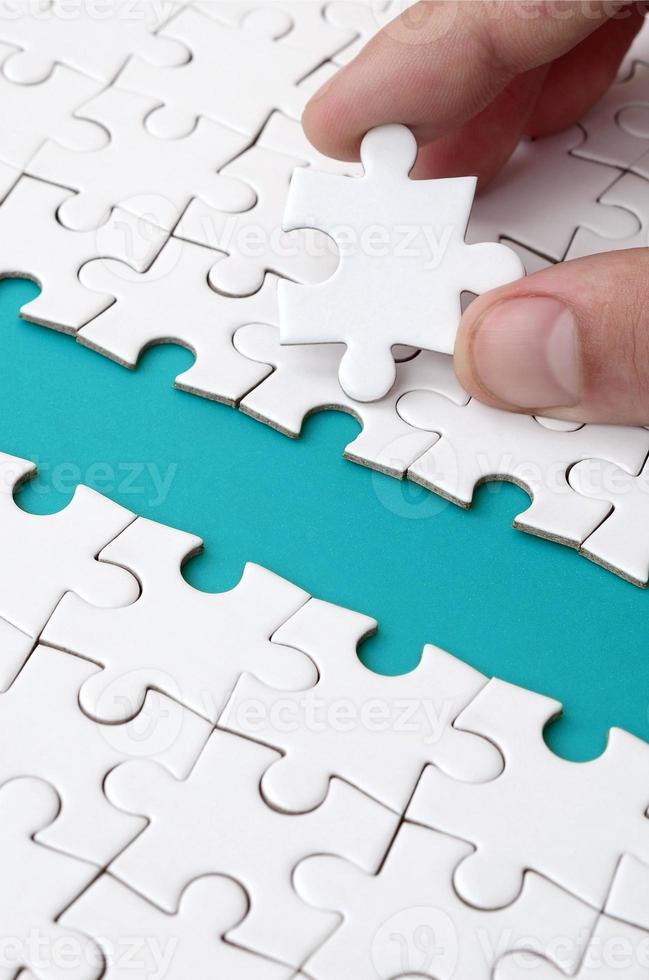 The human hand paves the way to the surface of the jigsaw puzzle, forming a blue space. The concept of overcoming the difficulties on the way to success photo