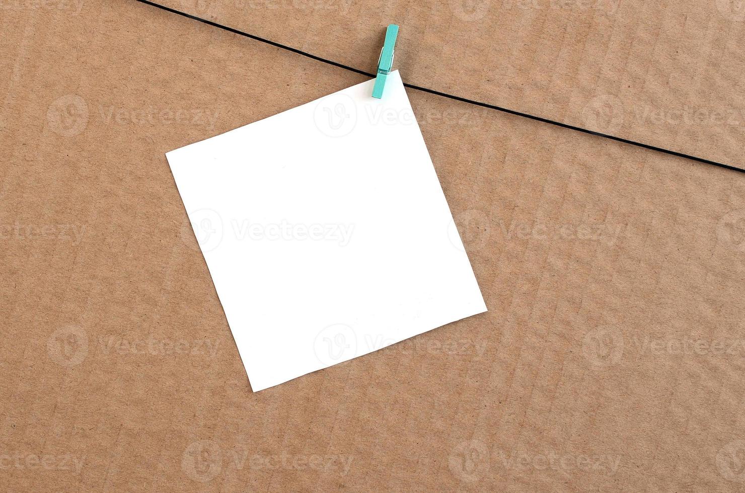 White blank card on rope on a brown cardboard background. Creative reminder, small sheet of paper on wooden clothespin, memo backdrop photo