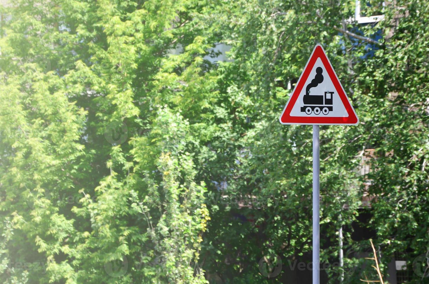 Triangular road sign with a picture of a black locomotive on a white background in a red frame. Warning sign for the presence of a railway crossing the motor road photo