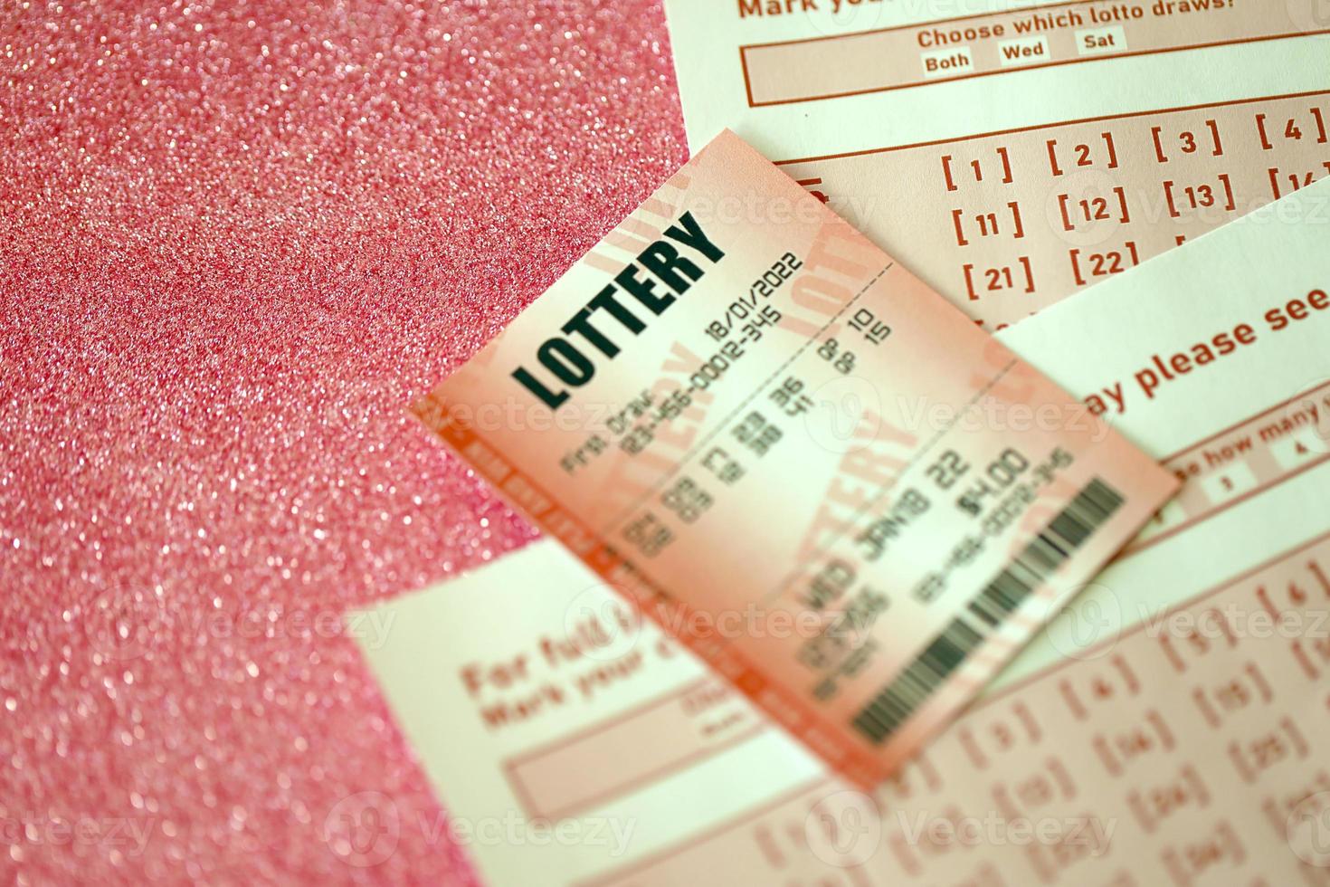 Red lottery ticket lies on pink gambling sheets with numbers for marking to play lottery. Lottery playing concept or gambling addiction. Close up photo