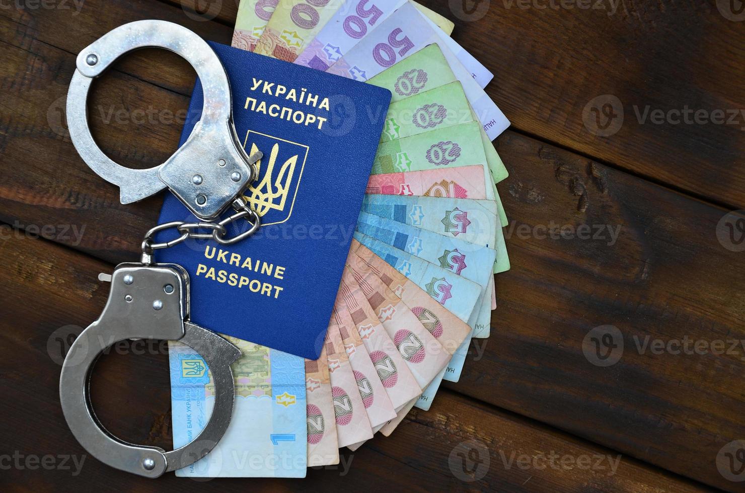 A photograph of a Ukrainian foreign passport, a certain amount of Ukrainian money and police handcuffs. The concept of arresting Ukrainian illegal immigrants while trying to bribe photo