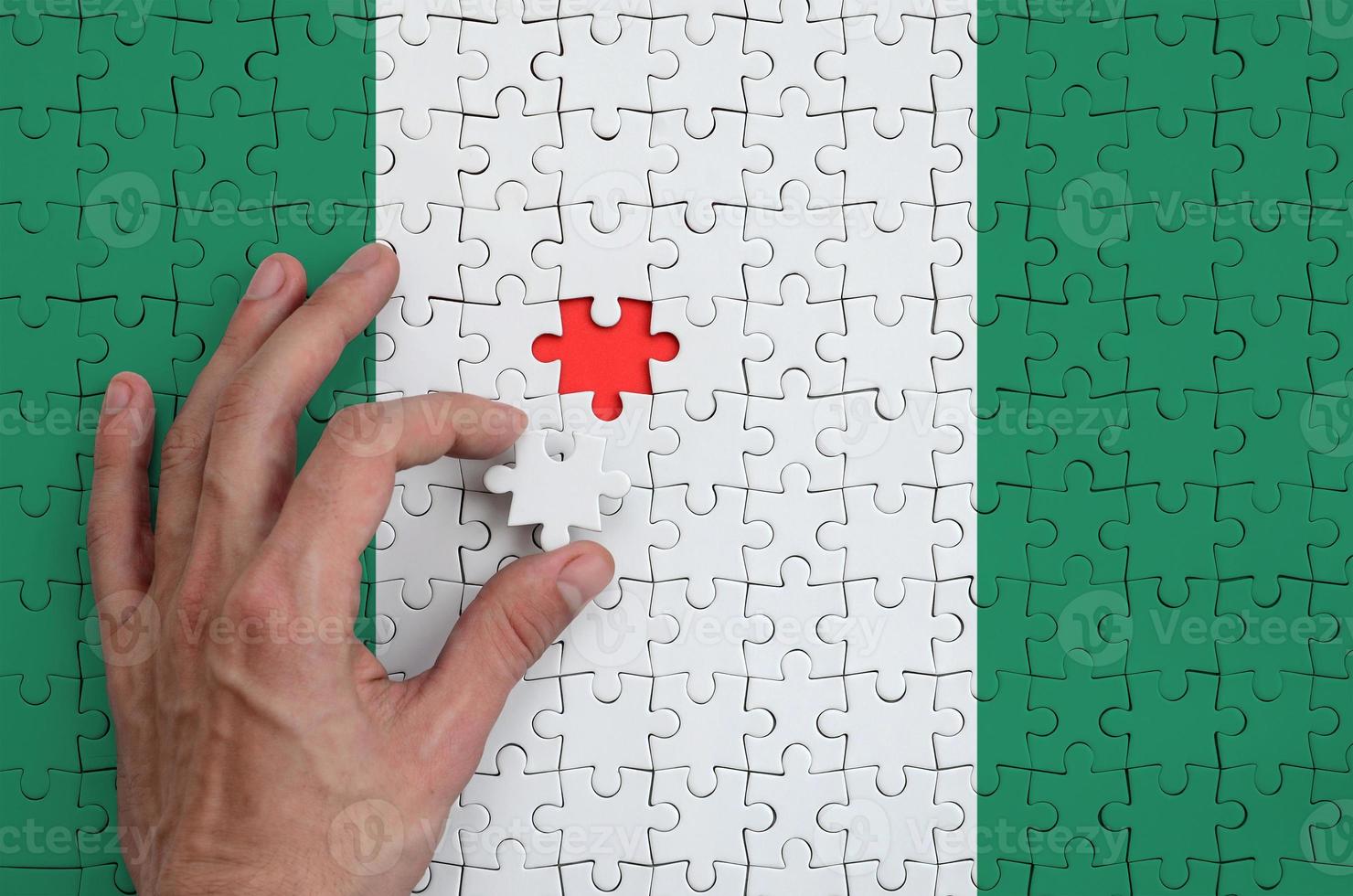 Nigeria flag is depicted on a puzzle, which the man's hand completes to fold photo