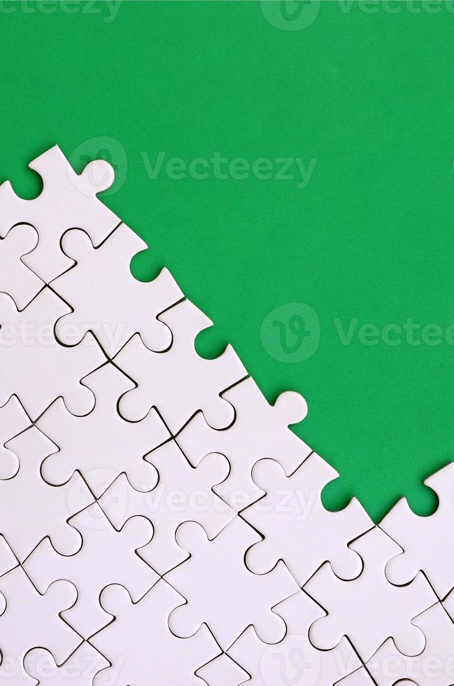 Fragment of a folded white jigsaw puzzle on the background of a green plastic surface. Texture photo with copy space for text
