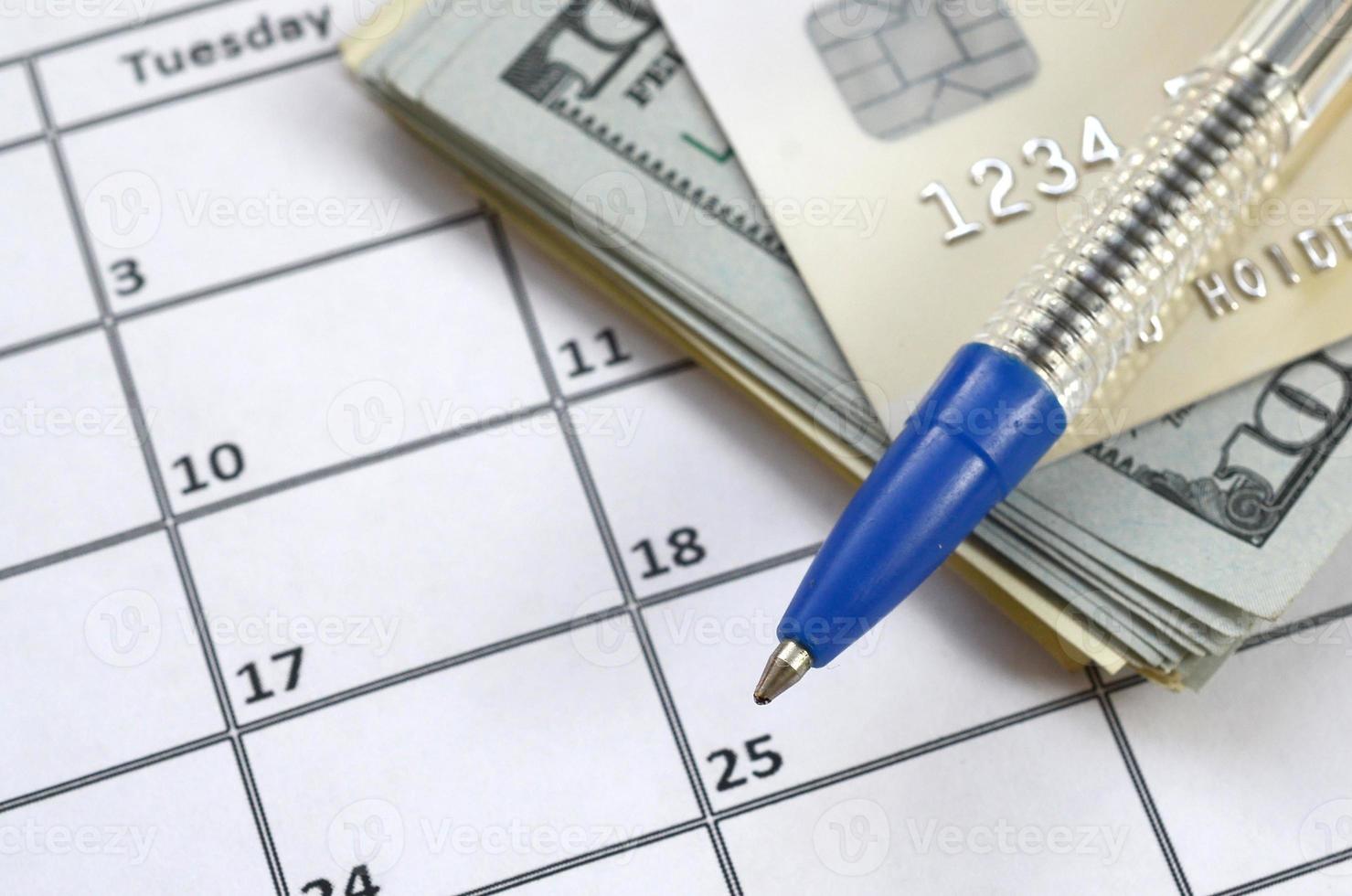 Pen and credit card on many hundred US dollar bills on calendar page close up photo
