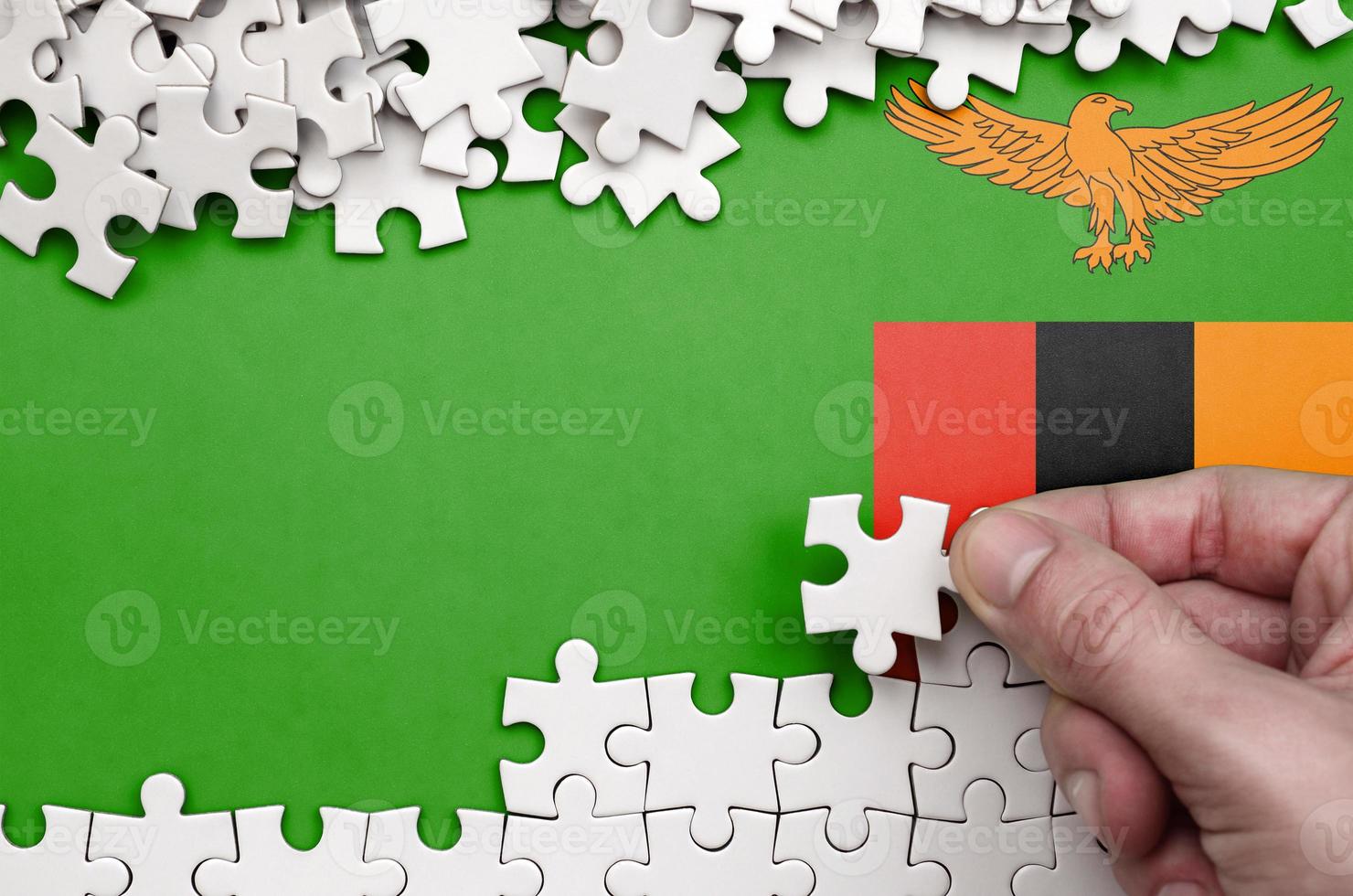 Zambia flag is depicted on a table on which the human hand folds a puzzle of white color photo