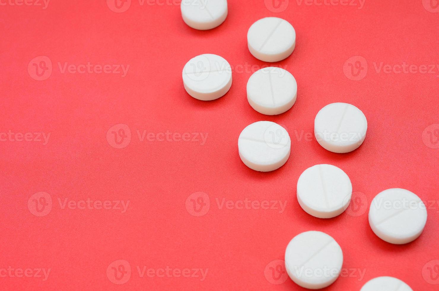 A few white tablets lie on a bright red background surface. Background image on medical and pharmaceutical topics photo