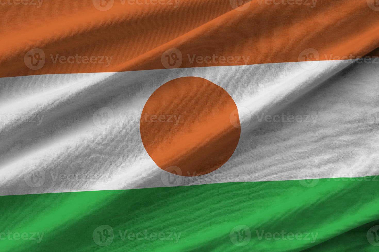 Niger flag with big folds waving close up under the studio light indoors. The official symbols and colors in banner photo
