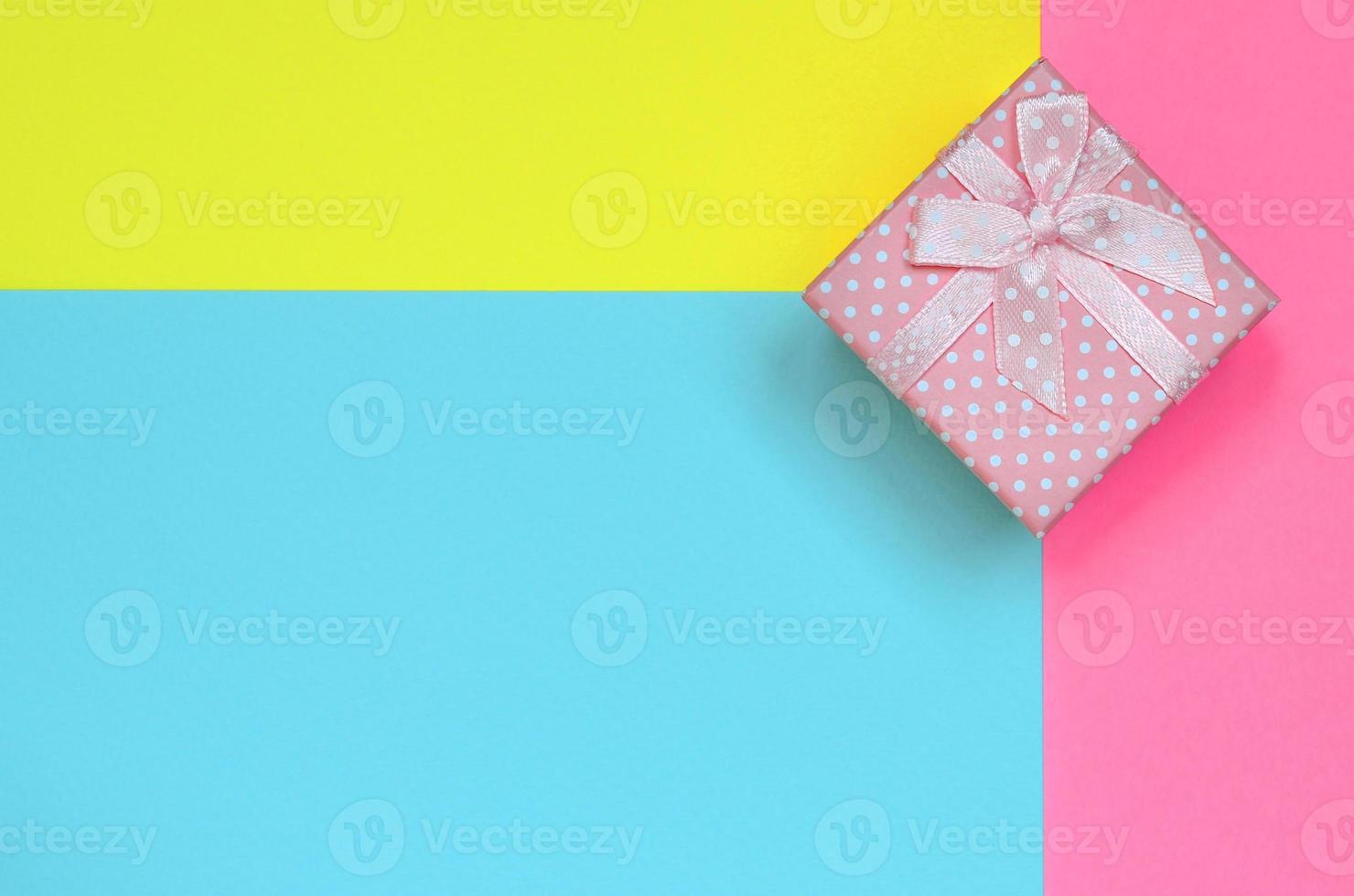 Small pink gift box lie on texture background of fashion pastel blue, yellow and pink colors paper in minimal concept photo