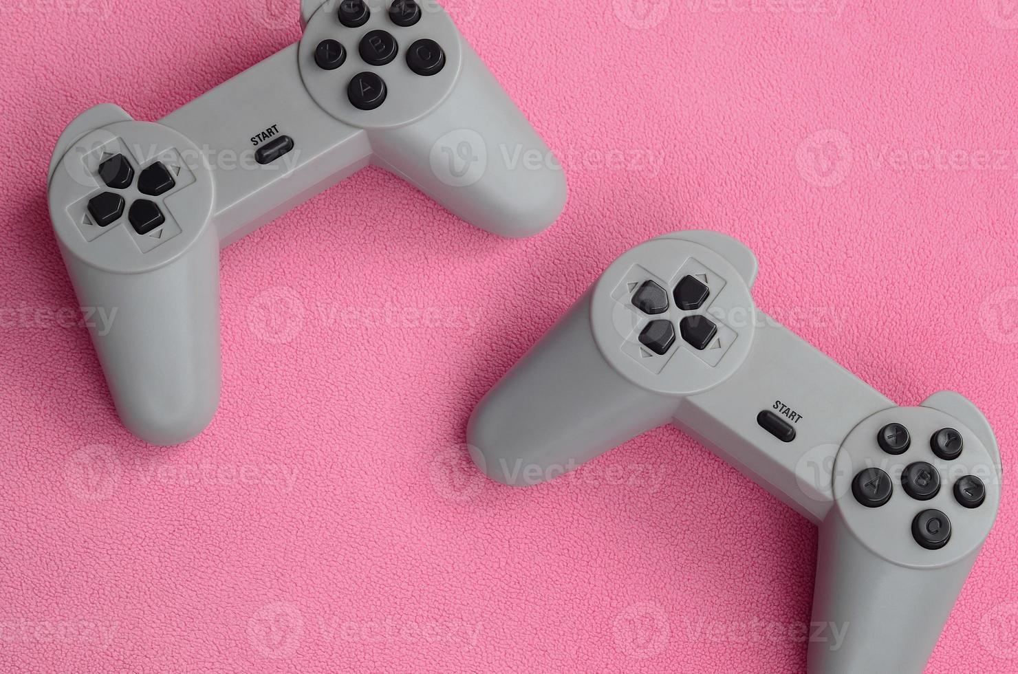 concepto de juegos. dos joysticks de almohadilla se encuentran sobre la manta de tela de lana rosa peluda. controladores para videojuegos en una textura de fondo de material de felpa suave rosa claro foto