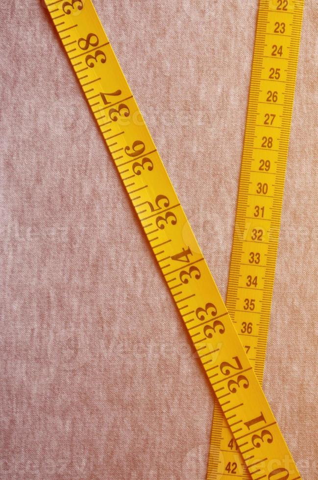 Yellow measuring tape lies on a gray knitted fabric photo