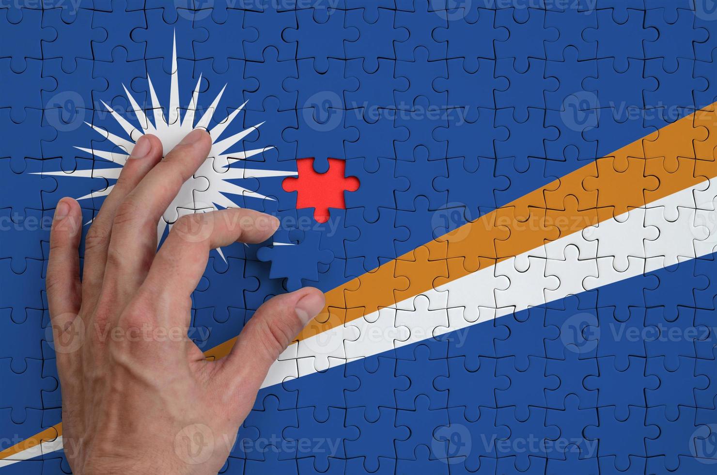 Marshall Islands flag is depicted on a puzzle, which the man's hand completes to fold photo