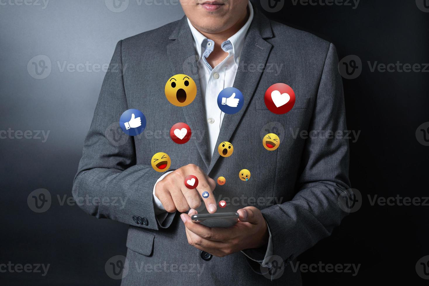 Close up businessman pushing, touching on smartphone with virtual emotion icon on black and gray background photo