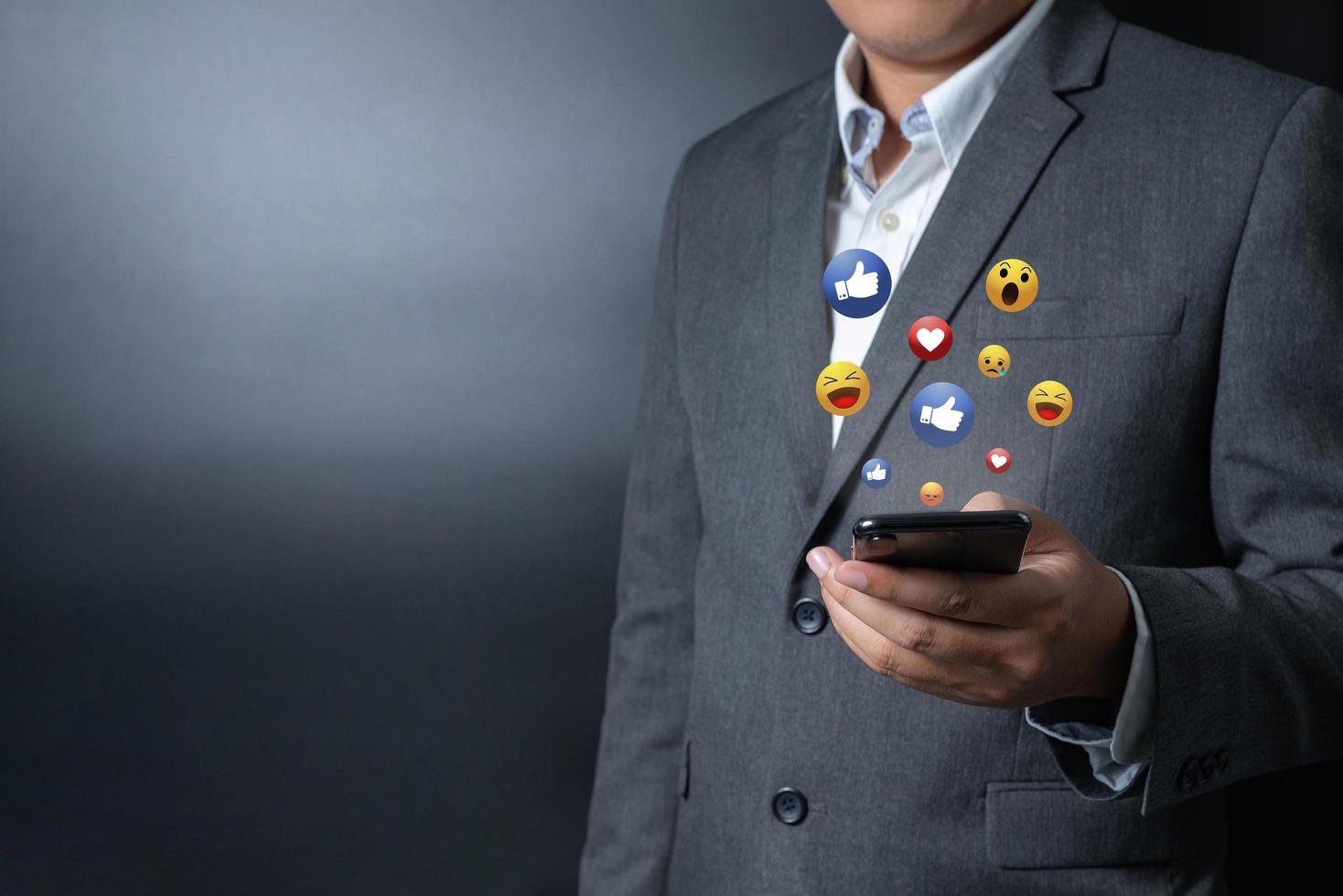 Close up businessman pushing, touching on smartphone with virtual emotion icon on black and gray background photo