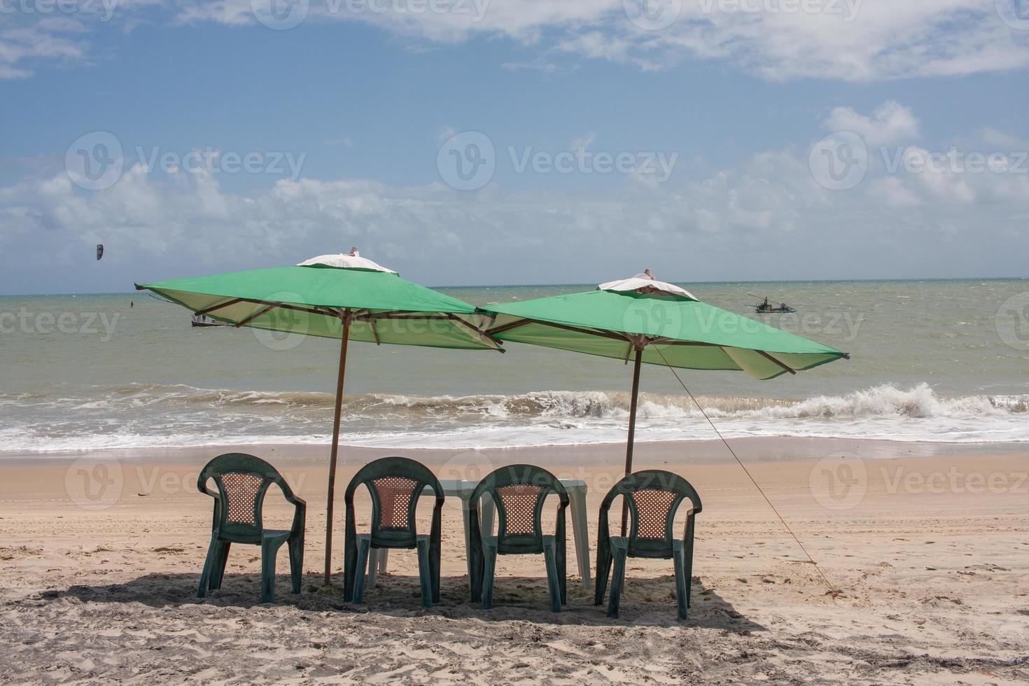 Two green umbrellas set up with a small table at the beach in Combuco, Brazil photo