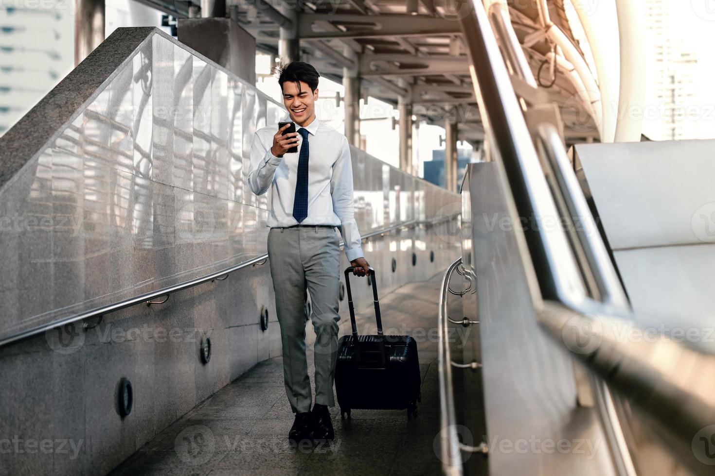 Smiling  Passenger Businessman Using Mobile Phone while Walking with Suitcase in the Airport or Public Transportation Station. Lifestyle of Modern People. Full Length photo