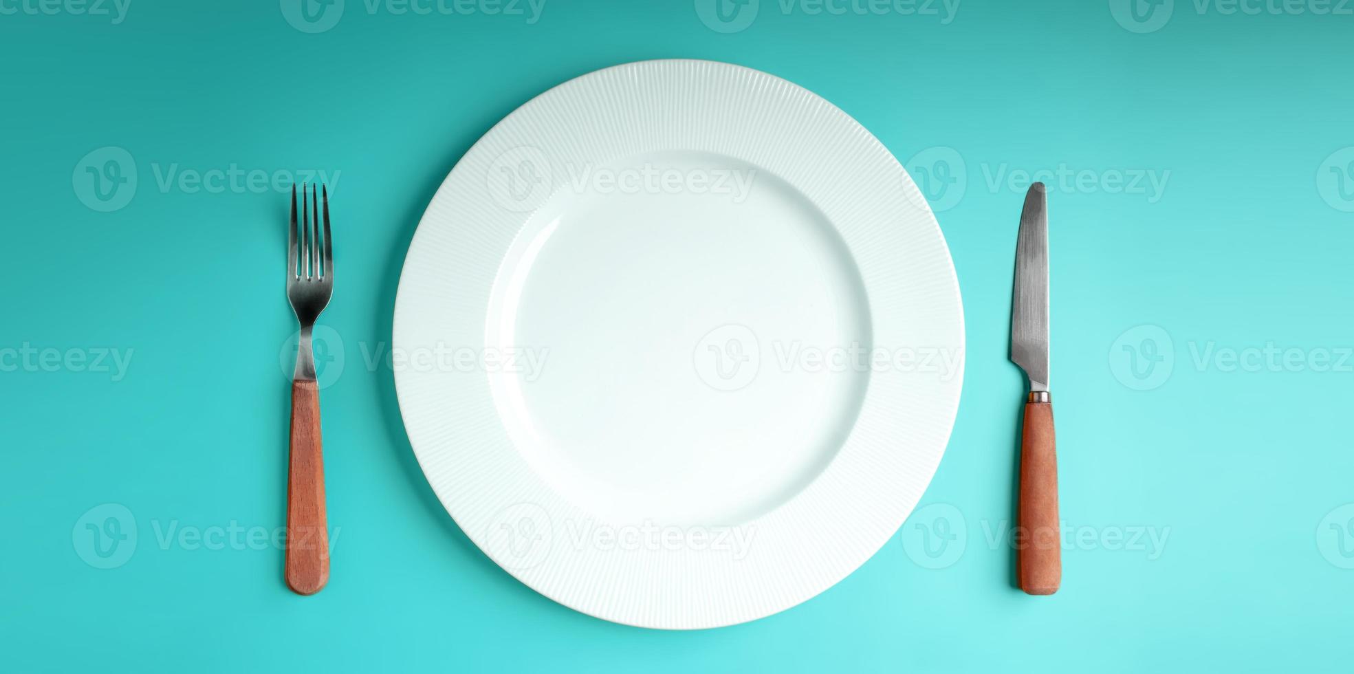 White Empty Plate with Fork and Knife Lay on Blue Table Background. Food Shortage, World Food Crisis Issue. Table Top View photo