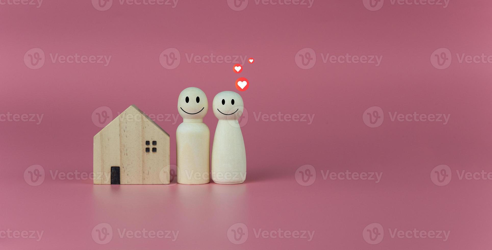 concepto de casa feliz. casa modelo con muñecas de madera alineadas sobre fondo rosa e íconos del corazón. indica felicidad y amor en el hogar. foto