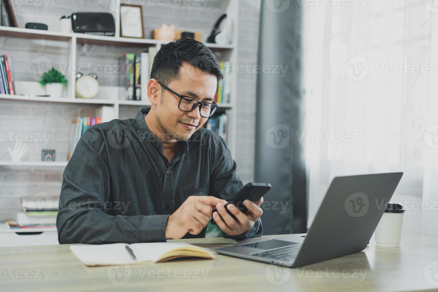 Man using smartphone after working with laptop on table, businessman using mobile phone to search or social media or shopping online or stock or crypto currency. Smart phone conversation conferrence. photo