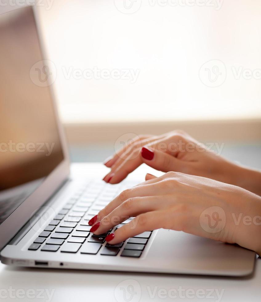 la chica detrás de la computadora portátil. manos femeninas escribiendo texto en el teclado mientras intercambian mensajes a través de las redes sociales usando una computadora portátil. una trabajadora de oficina revisa su correo electrónico mientras está sentada en un escritorio foto