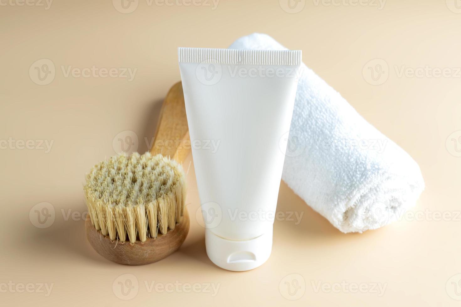 SPA cosmetics, woman body and skincare products on beige background. Natural bristle dry massage brush and body or face cream in white plastic tube. Eco-friendly and zero waste concept. photo