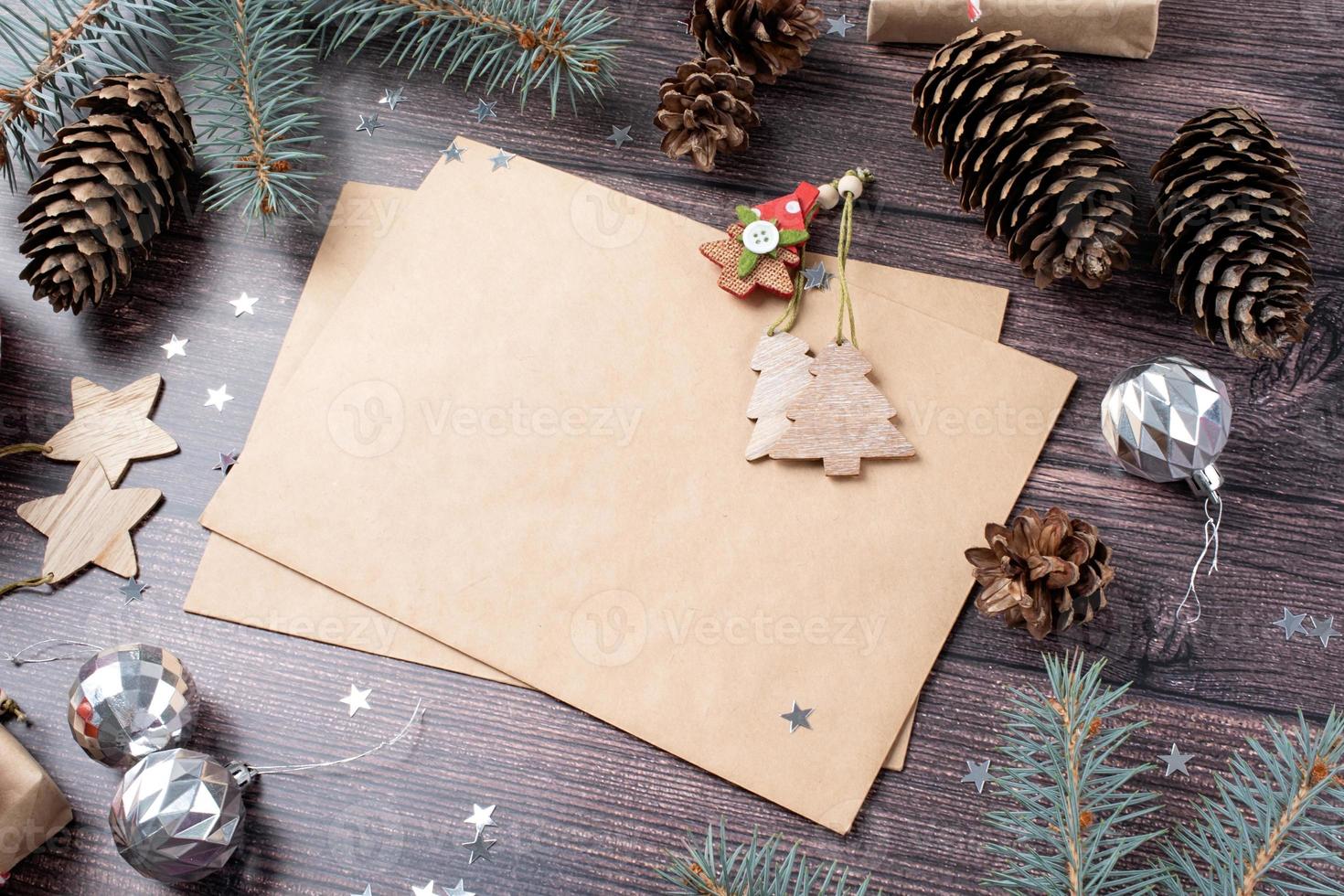 sobre artesanal con adornos navideños y conos de pino vista de ángulo alto sobre fondo de madera foto