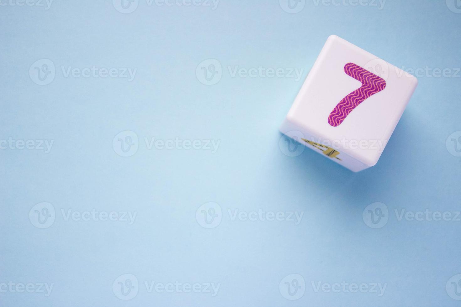 Close-up photo of a white plastic cube with a violet number 7 on a blue background in the upper right corner. With copy space