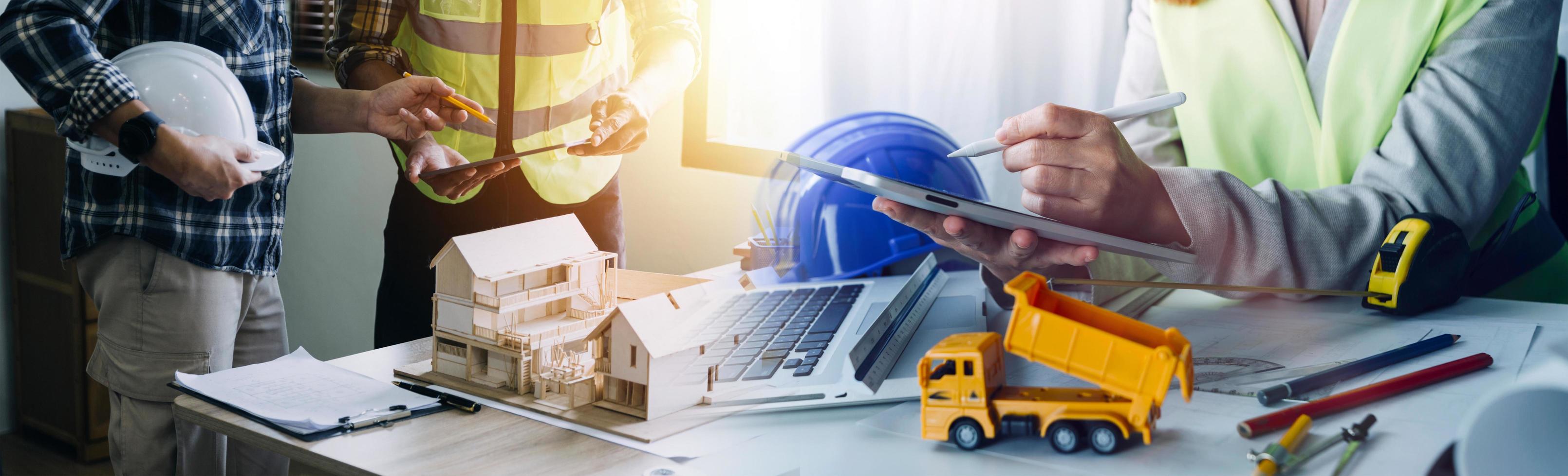 Two colleagues discussing data working and tablet, laptop with on on architectural project at construction site at desk in office photo