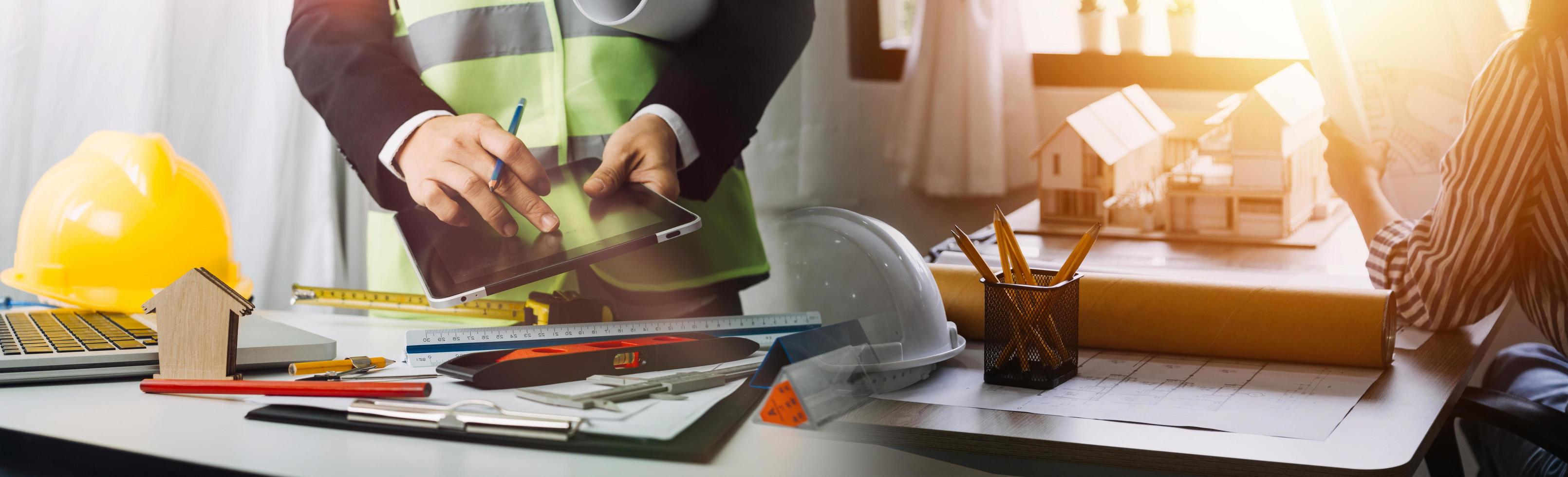 Two colleagues discussing data working and tablet, laptop with on on architectural project at construction site at desk in office photo