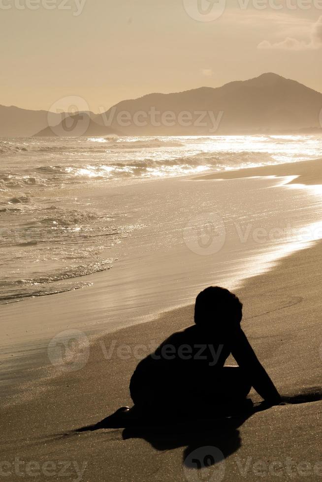 Rio de Janeiro, RJ, Brazil, 2021 - A boy in silhouette plays with sand at sunset on Barra Beach photo