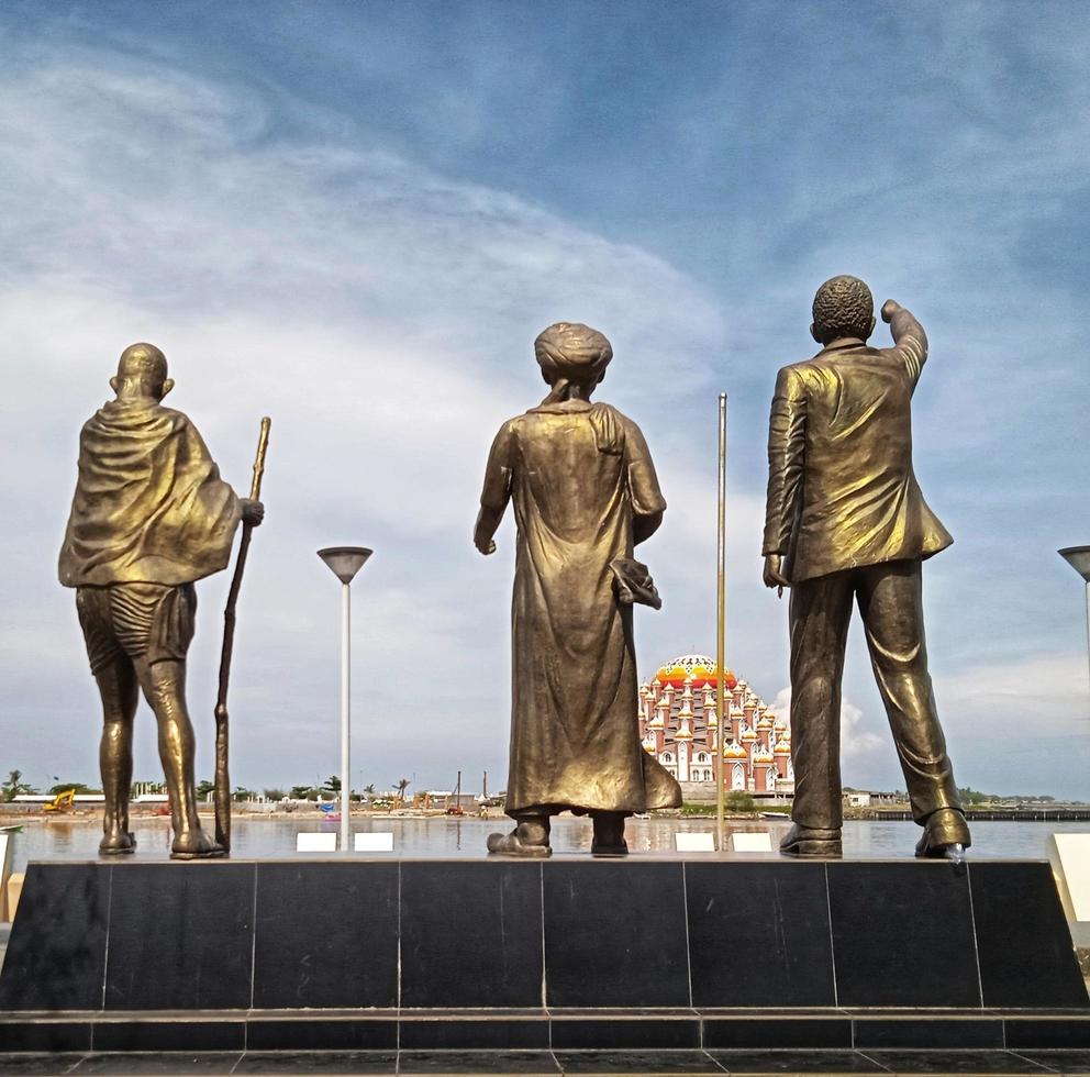 Makassar,Indonesia,31 Juni 2021-three people statue golden color overlooking the mosque in the middle of the sea with a sky blue background photo