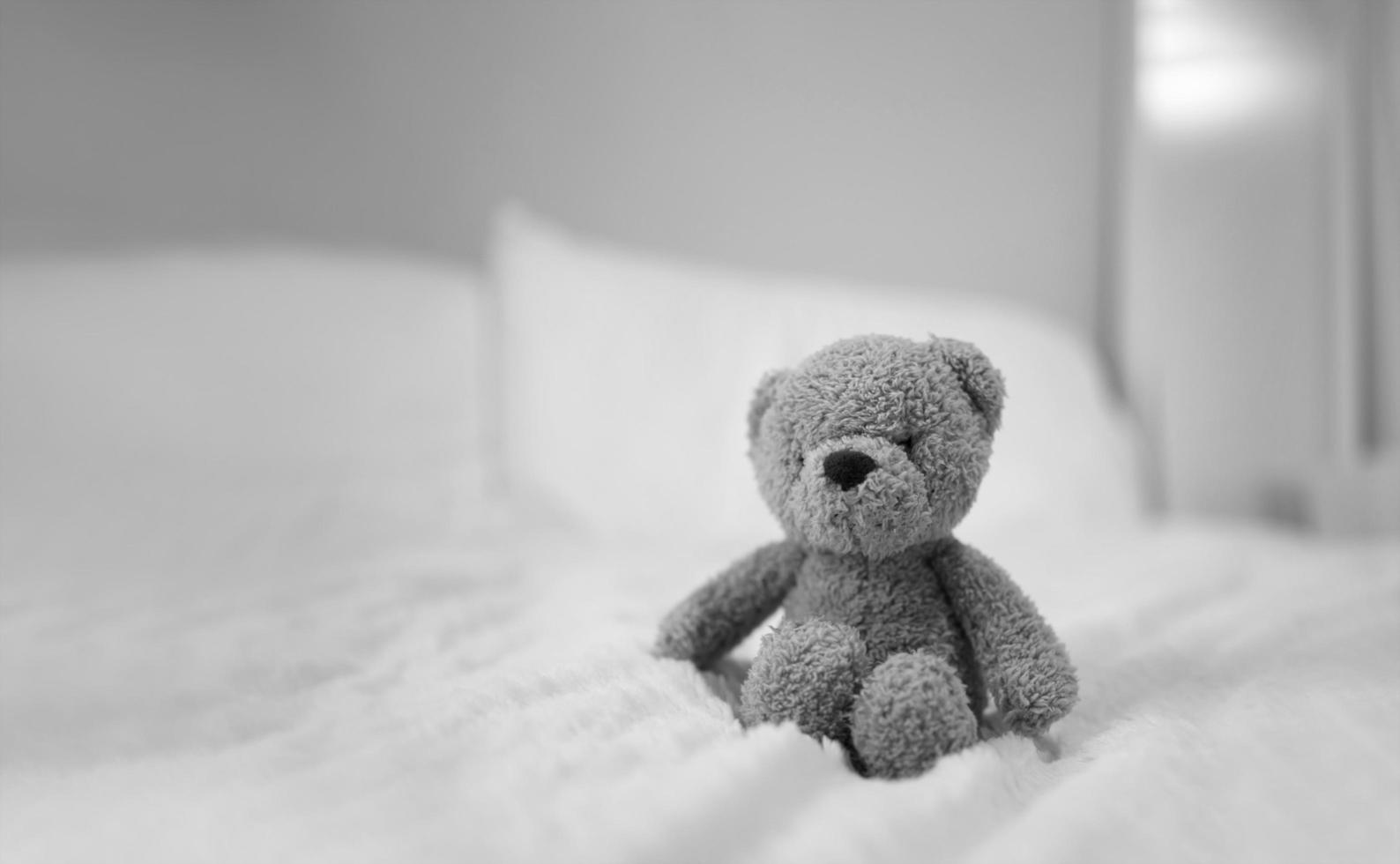 oso de peluche sentado en la cama en el dormitorio, oso marrón solitario blanco y negro que se queda solo en casa, concepto de soledad, día internacional de los niños desaparecidos foto