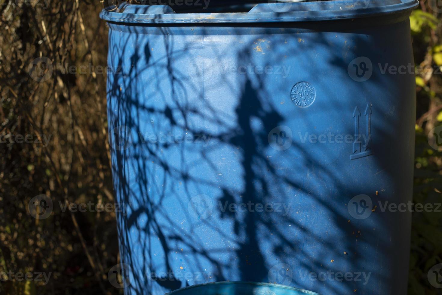 barril de agua azul en el jardín. barril azul y sombra de las plantas. contenedor de plástico. foto