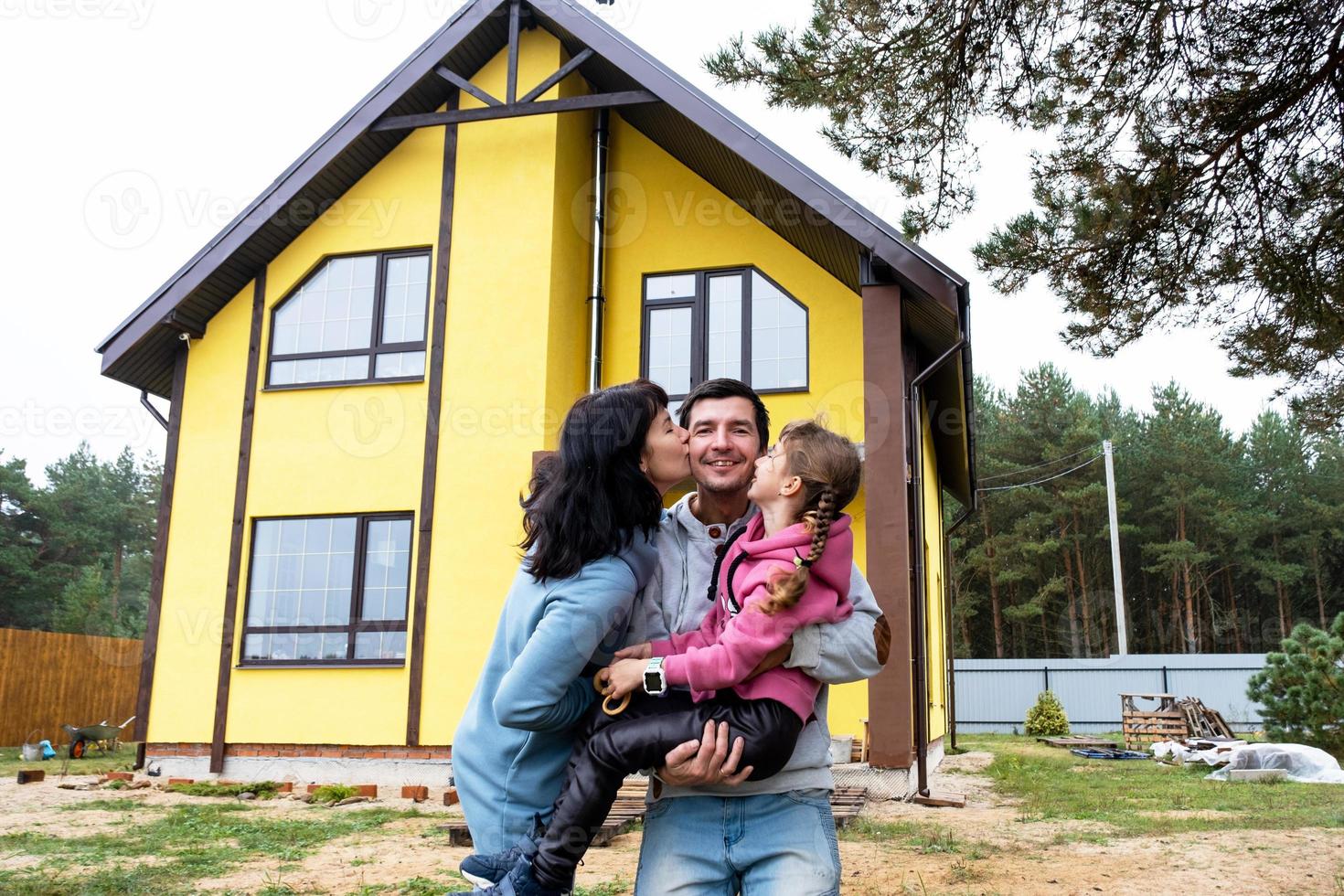 familia feliz en el patio de una casa sin terminar - compra de una cabaña, hipoteca, préstamo, reubicación, construcción foto