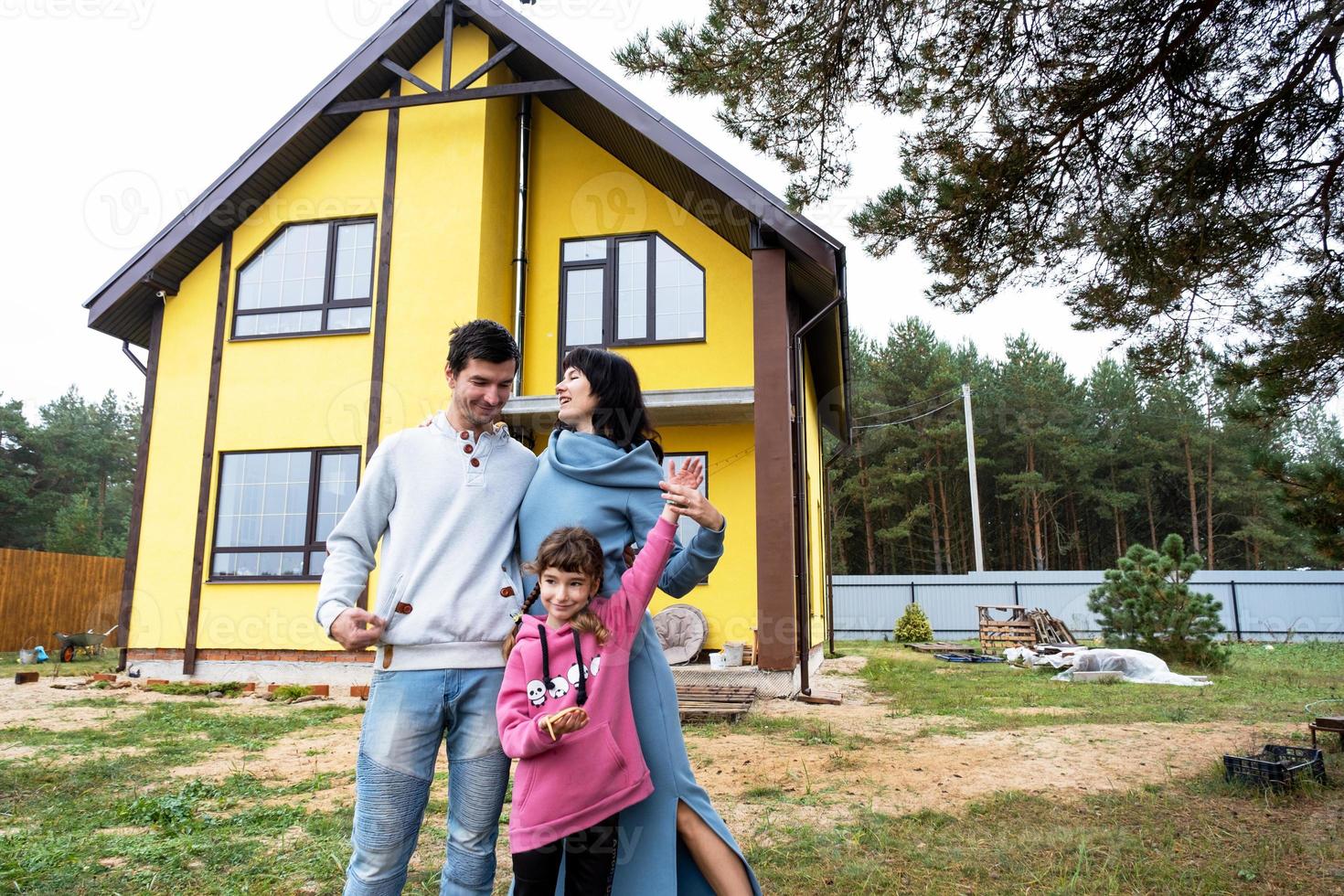 familia feliz en el patio de una casa sin terminar - compra de una cabaña, hipoteca, préstamo, reubicación, construcción foto