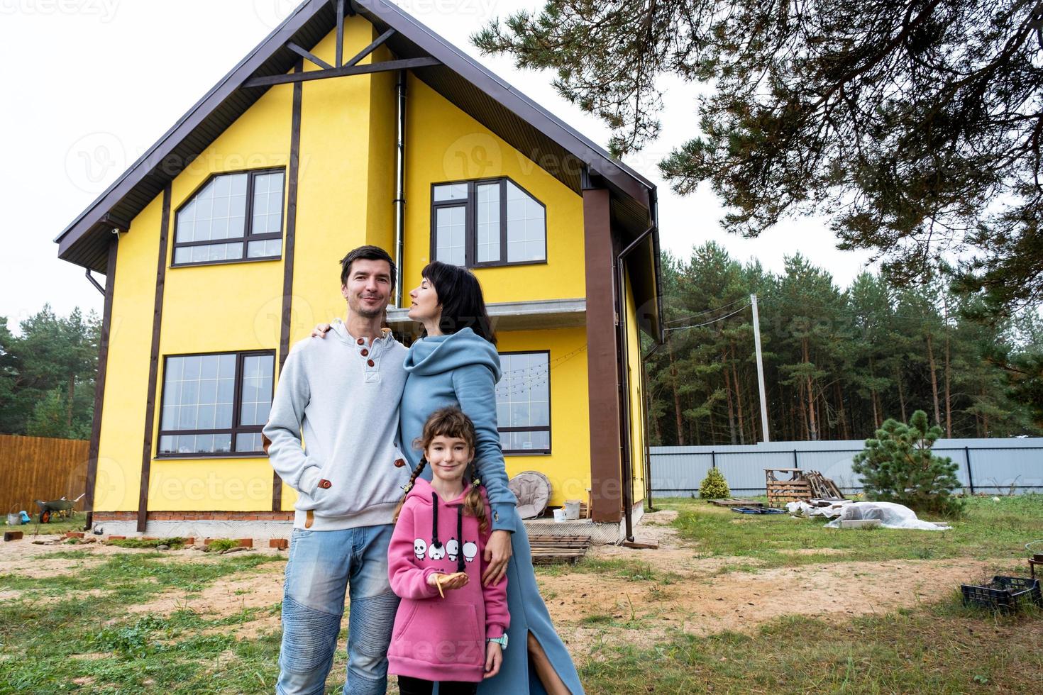 Happy family in the yard of an unfinished house - purchase of a cottage, mortgage, loan, relocation, construction photo