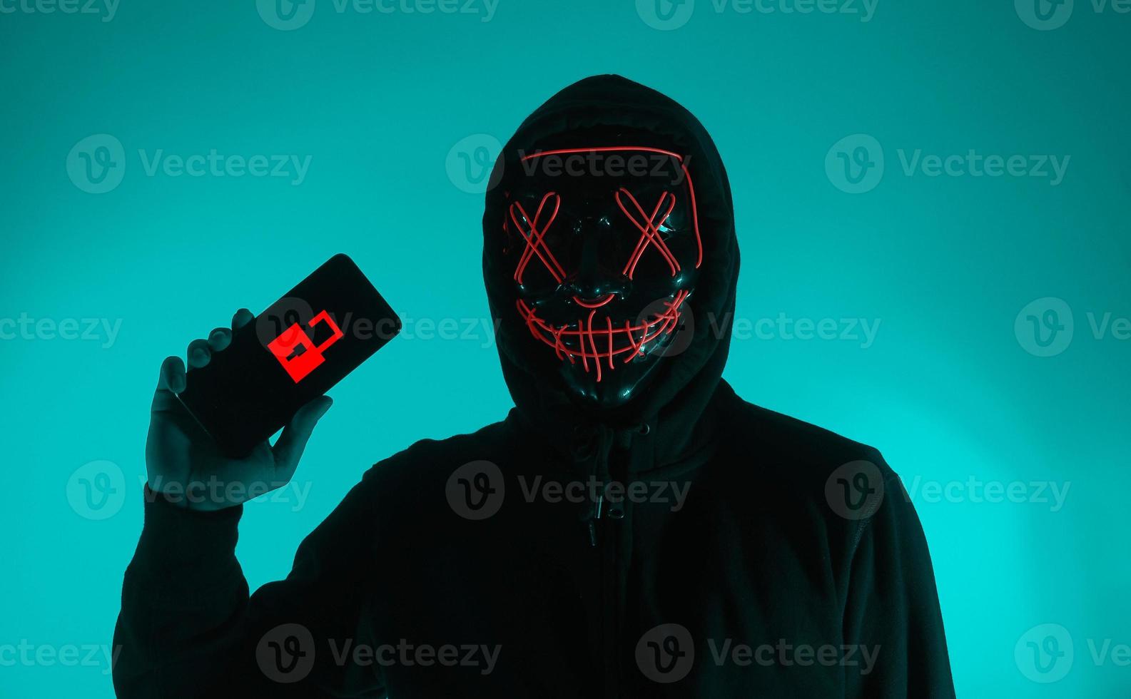 Digital security Concept. Anonymous hacker with mask holding smartphone hacked. photo