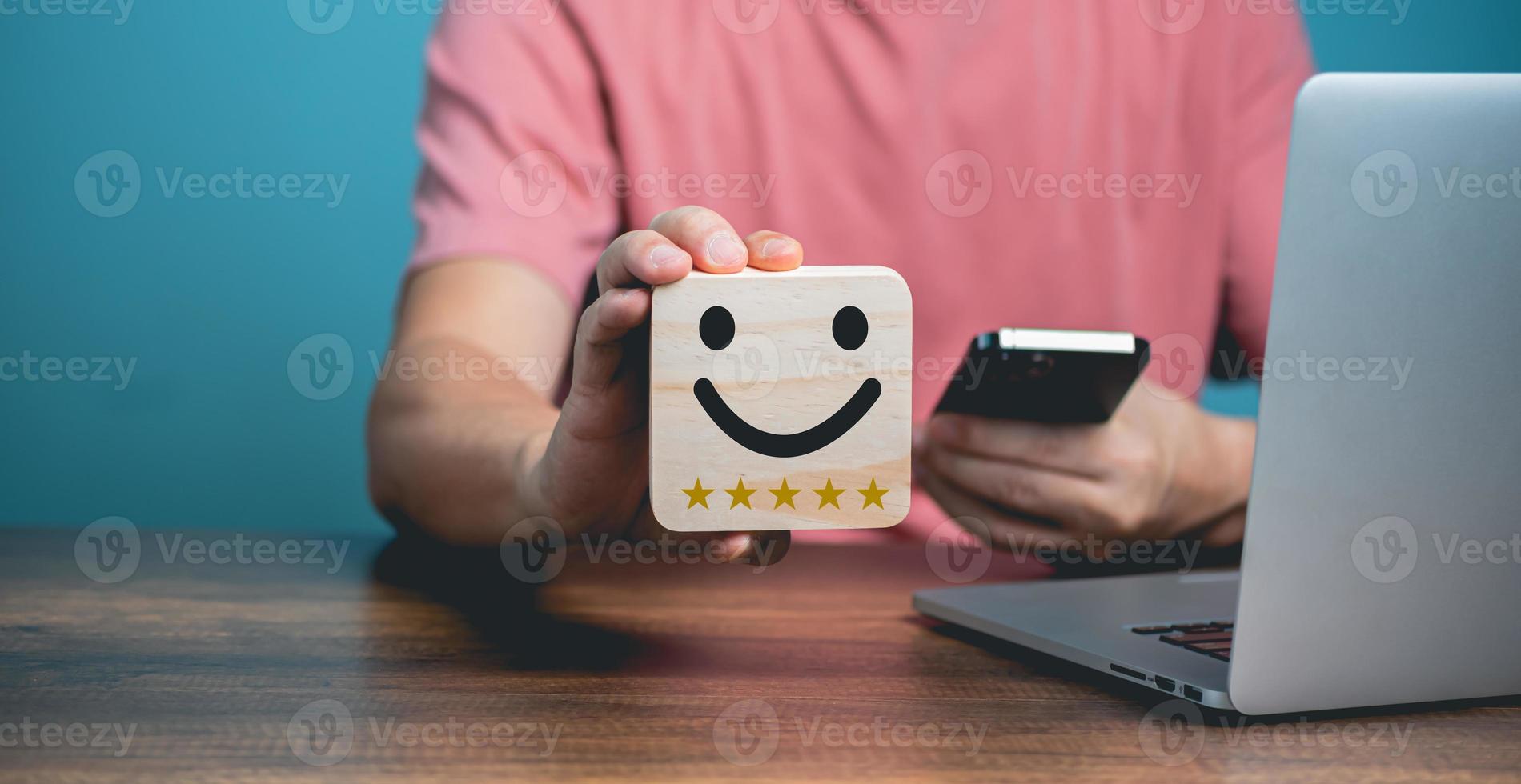 Customer service satisfaction concept, Young businessman using Mobile Phone and holding happy face wooden  with smiling face, satisfaction five stars rating icon. photo