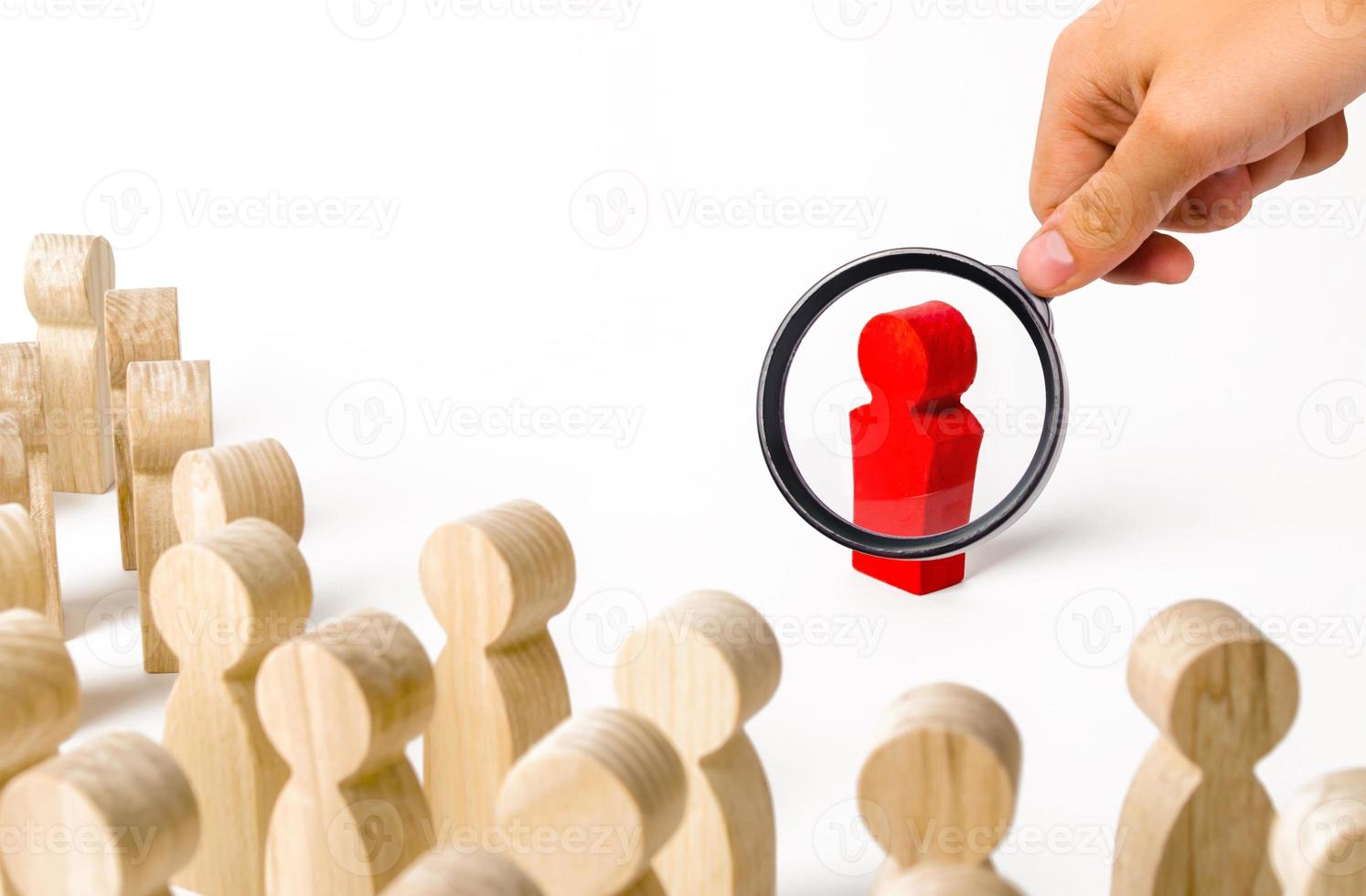 A magnifying glass looks at a red figurine of a man near a crowd. Leader, leadership and initiator of action. work or business organization. team building. Idol and example to follow. Distrust photo
