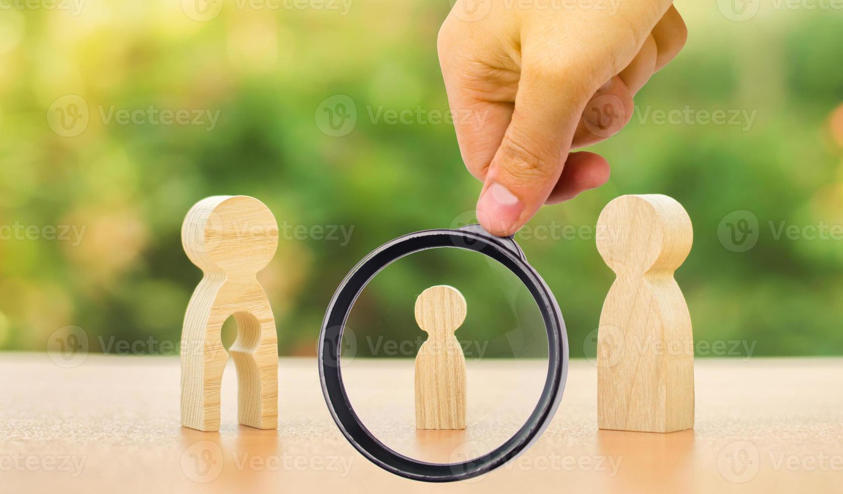 A magnifying glass looks at a childs figure stands between father and mother. The child chooses which parent to live with after their divorce. Guardianship over child. interest of child photo