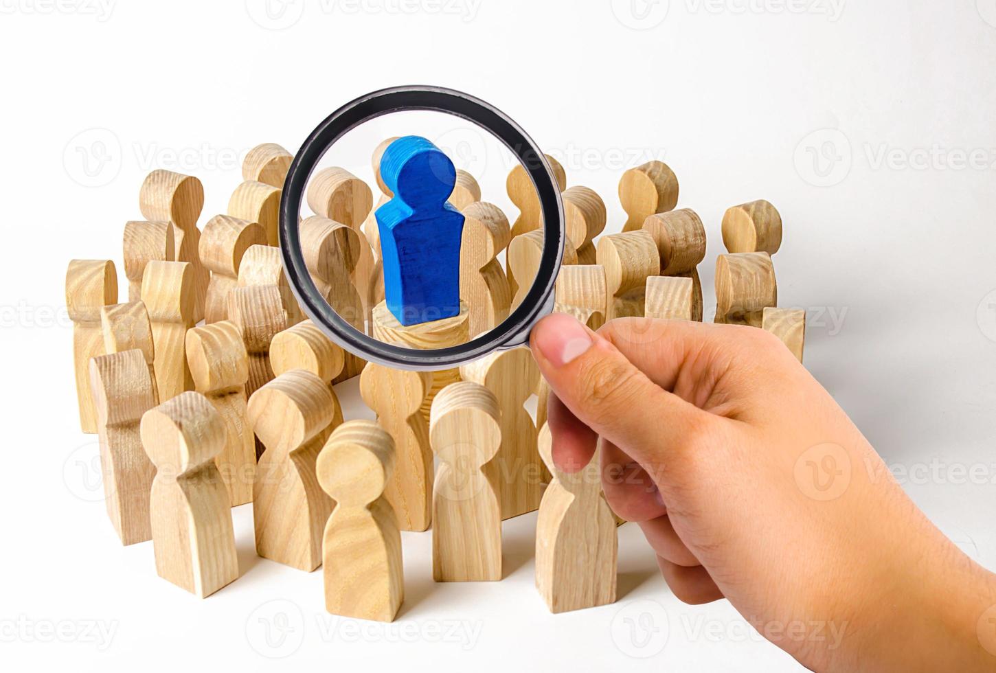 A magnifying glass looks at the blue figure of a man in the center of a crowd of people. Leadership and team management, an example for imitation. Loyalty and trust. Idol followers photo