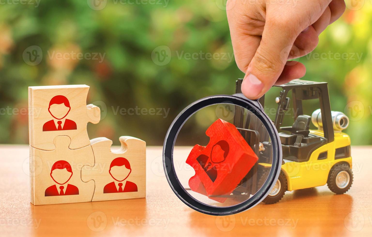 A magnifying glass looks at a forklift truck carries a red puzzle to the unfinished assembly of business team. Search, recruitment staff, hiring leader. Creating efficient and productive business unit photo