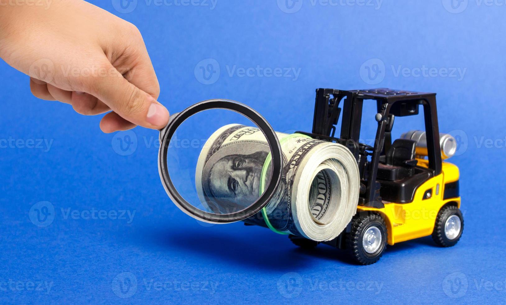 A magnifying glass looks at a forklift truck carries a bundle of dollars. Attracting direct investment in business and production, improving economic performance. capitalism. Export of capital photo