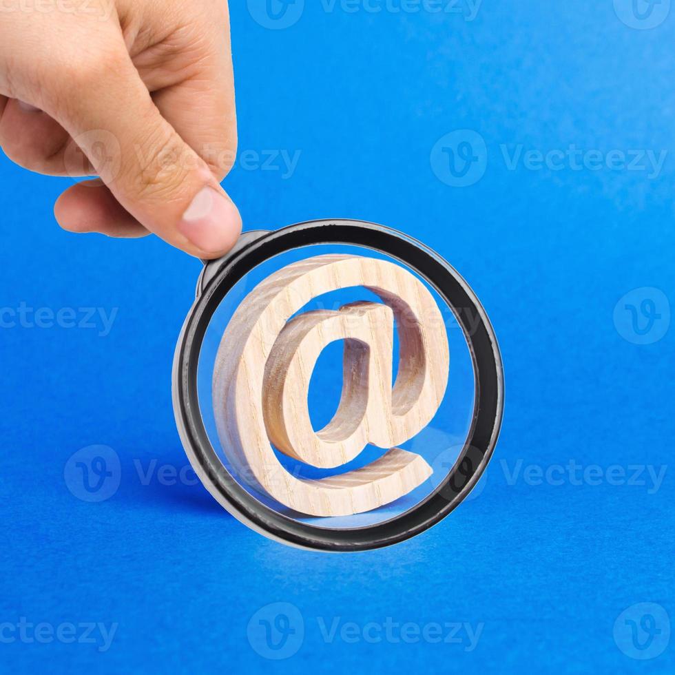 A magnifying glass looks at a email icon on blue background. internet correspondence. Contacts for business. Business tools. Internet and global communication, digitalization of economy. at commercial photo