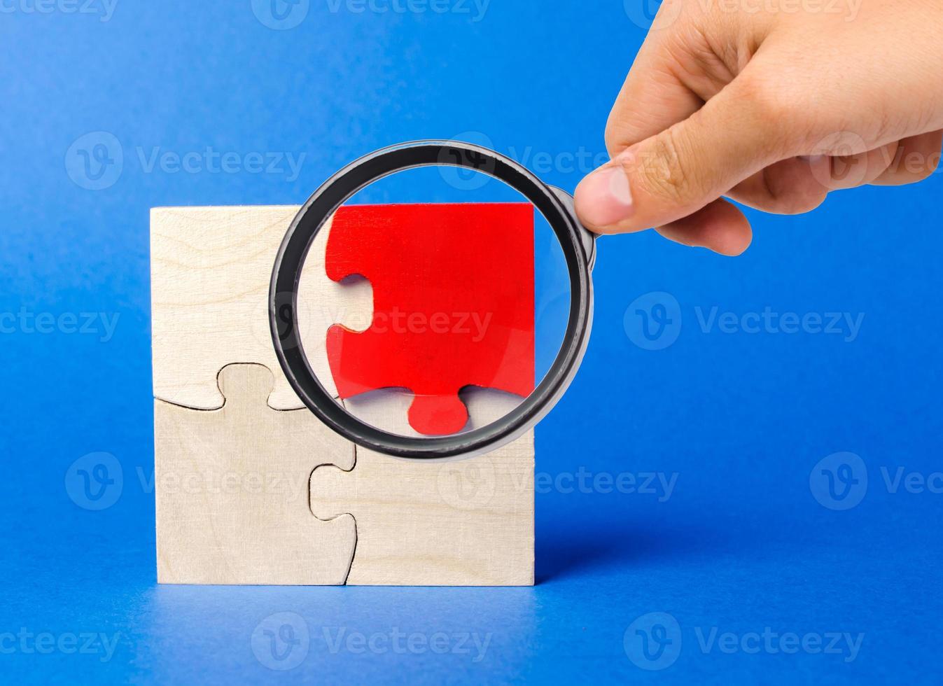A magnifying glass looks at a red wooden puzzles on a blue background. Individual opinion. Stand out from the crowd. Uniqueness. Divergent views. Different concepts to other people. photo